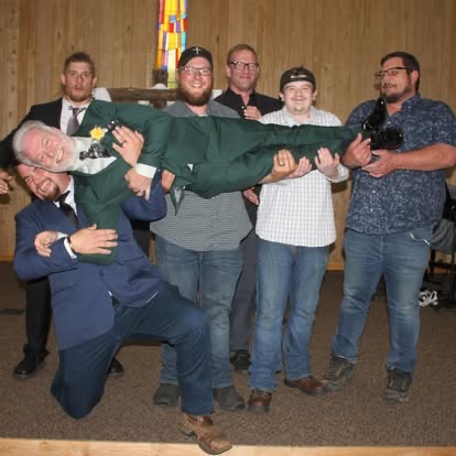 A group of men in the chapel joyfully lifting one man horizontally over their shoulders in celebration.