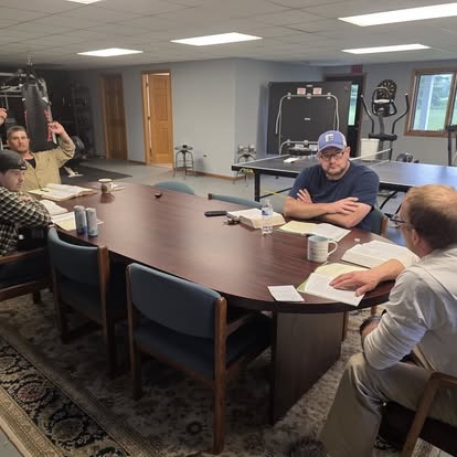 Men meeting around a conference table for study and discussion in a room with exercise equipment.