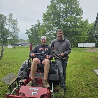 Two men with a Ferris zero-turn mower on the green grounds of His House of Hope on an overcast day.