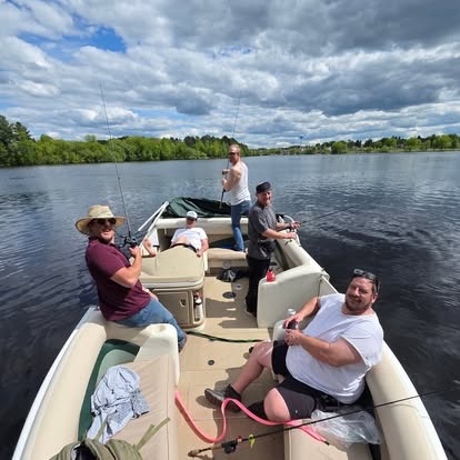 A group of men fishing together from a pontoon boat on a calm lake with cloudy skies overhead.