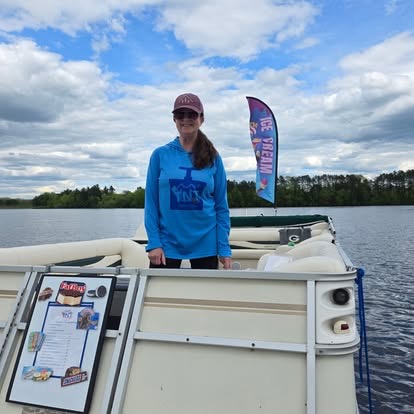 A woman standing on a pontoon boat on a northern Wisconsin lake with a fishing charter flag behind her.