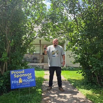 A supporter standing beside a Proud Sponsor of His House of Hope yard sign