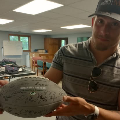 A man holding a signed Green Bay Packers commemorative football inside the house.